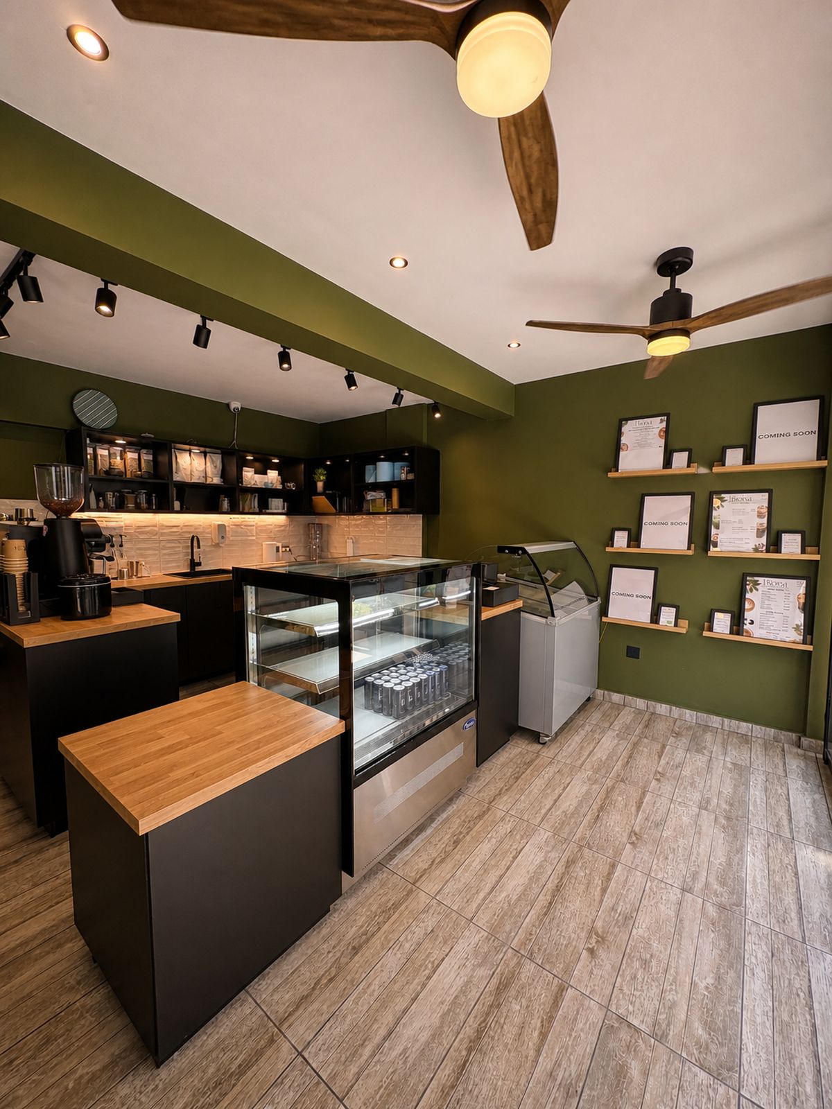 The Biora bar: grinder, espresso machine and cold case against an olive-green wall