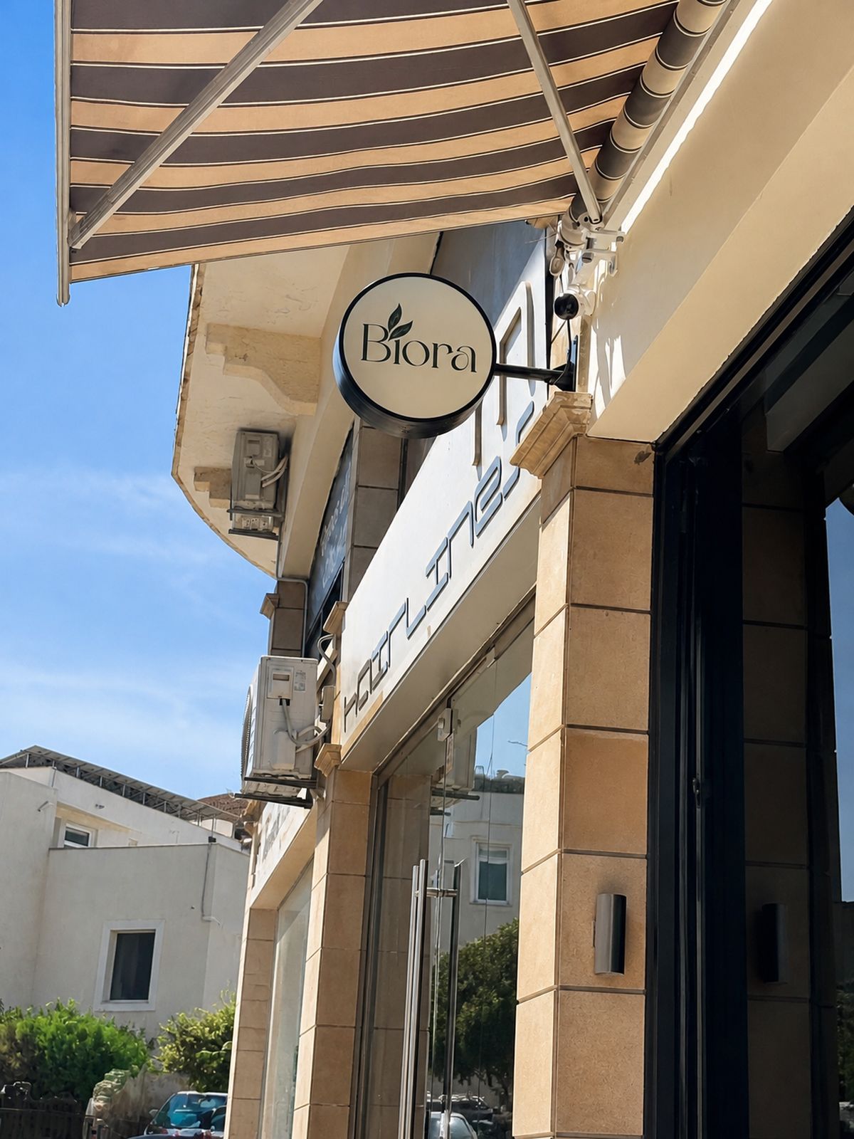 The round Biora sign above the pavement, beside the Hairlines salon